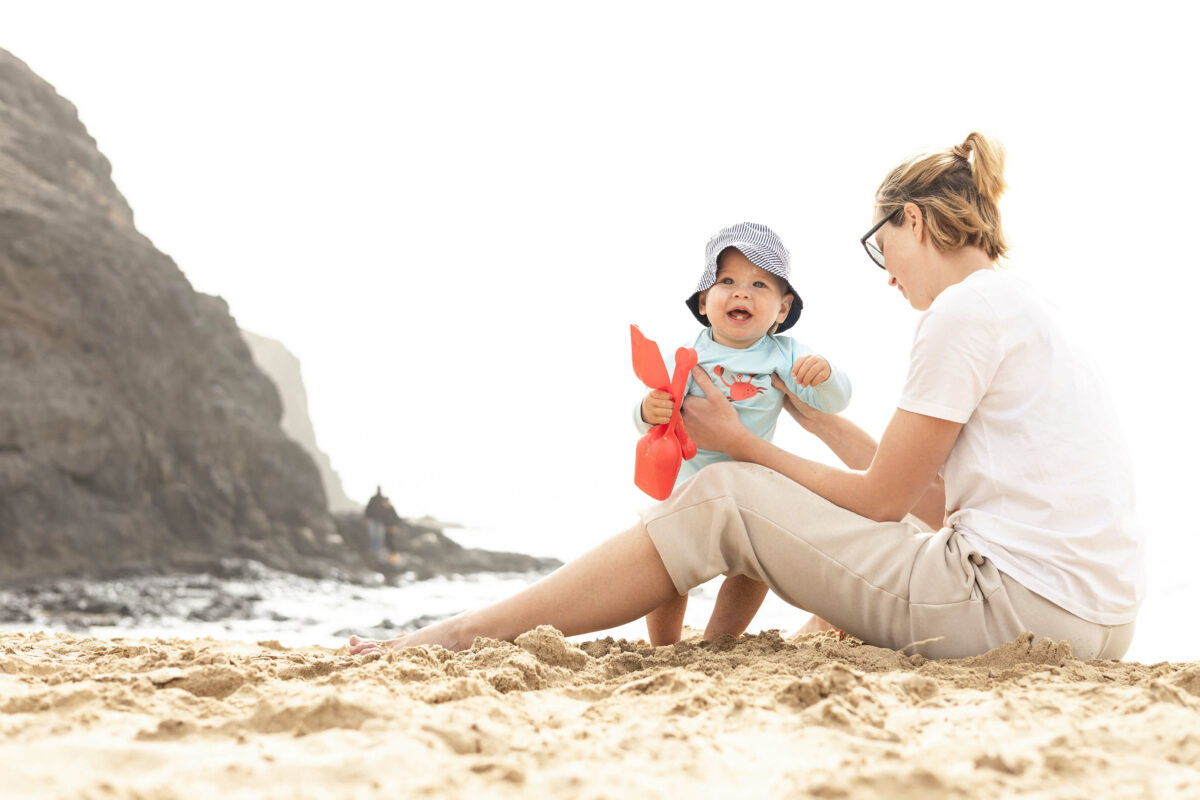 Mutter mit lachendem Baby im Familienurlaub am Strand