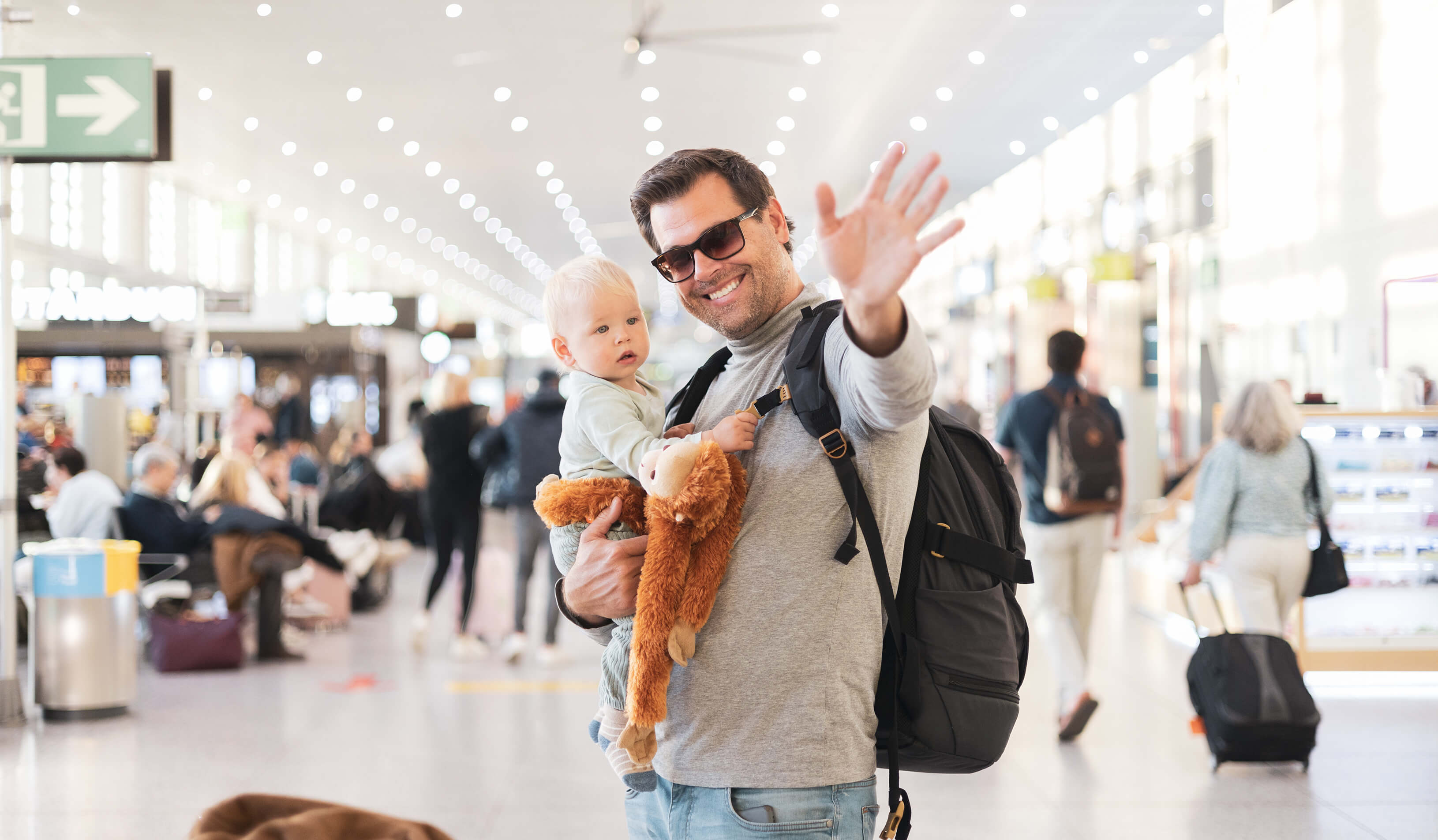 Winkender und lächelnder Vater mit Baby im Flughafen