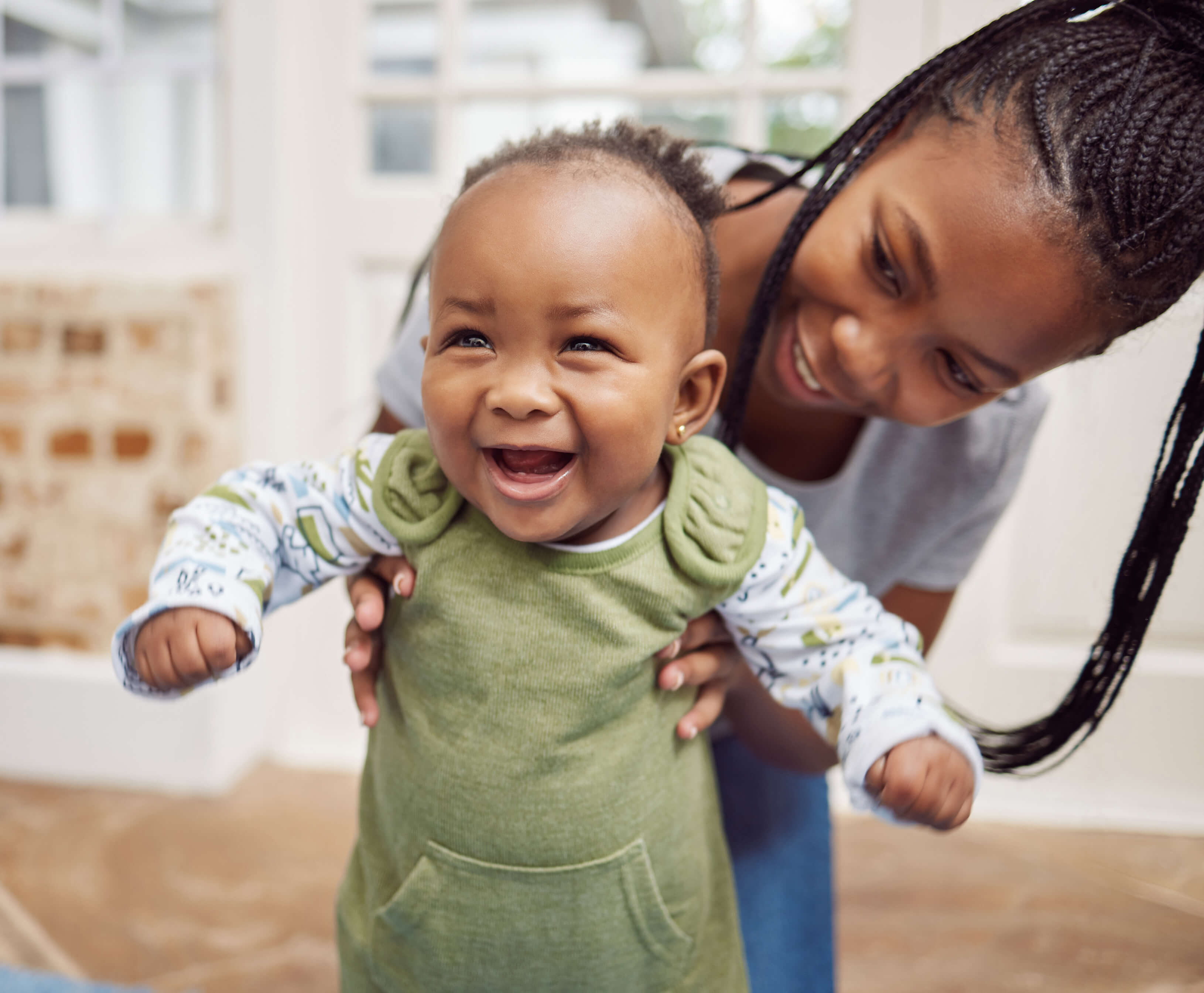 Ein Baby lernt laufen, seine Mutter hält es und beide lachen: Entwicklungskalender