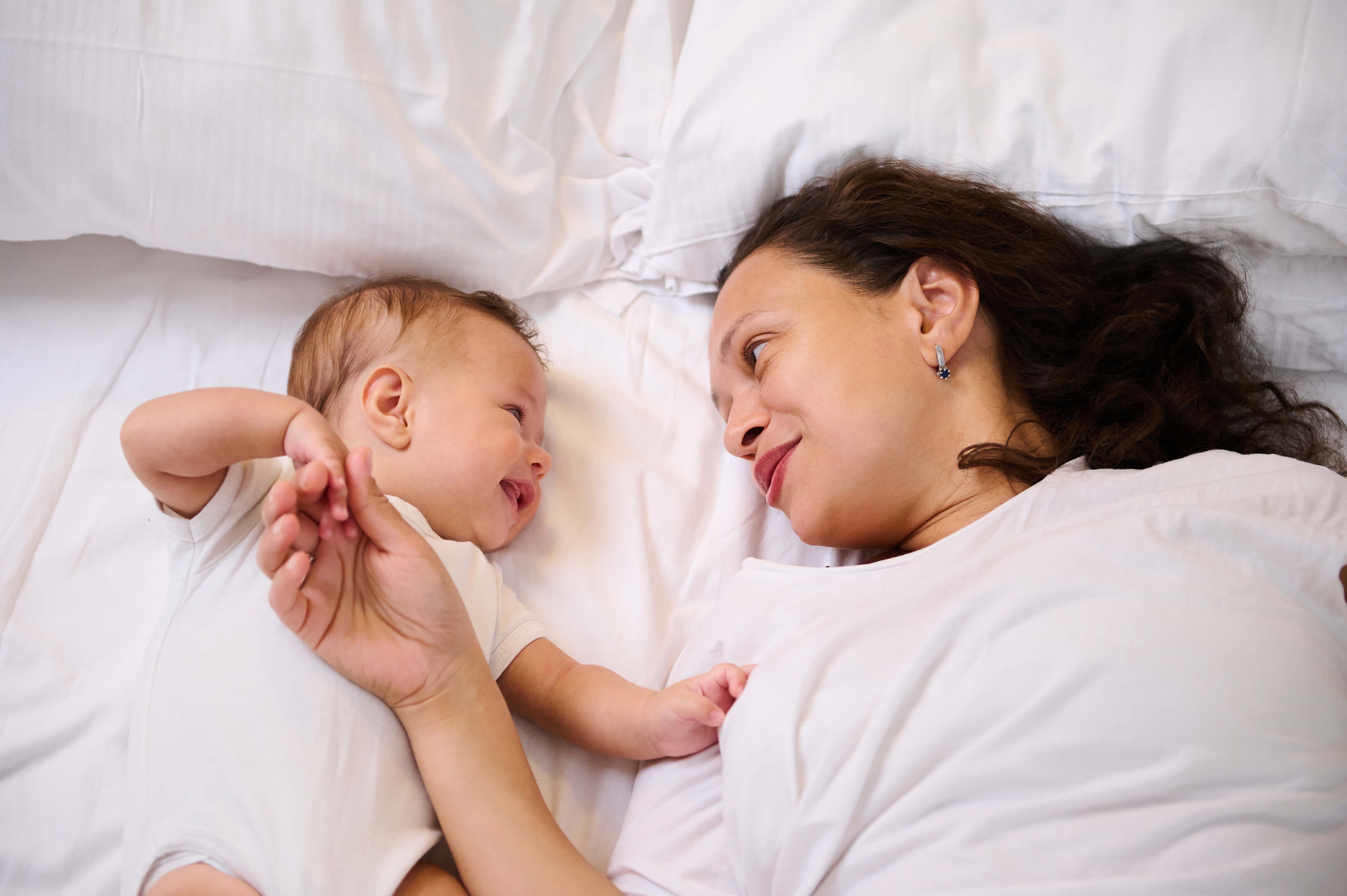 Mutter und Baby, das Kind lacht, beide halten Händchen